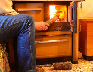 elderly person puts a piece of wood into the fire of the old wood-burning stove