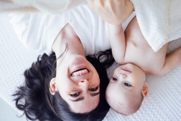Pretty infant in a white bodysuit with his mom on a light background.