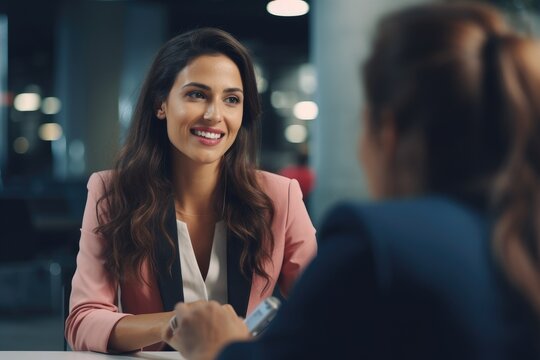 Smiling businesswoman sitting at table in office and talking to colleague, businesswoman giving interview to journalist in office, AI Generated