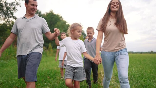 family walking on the grass in the park and holding hands. happy family childhood dream concept. a large family walks across the clearing and lifestyle talks to each other. outdoor nature walk