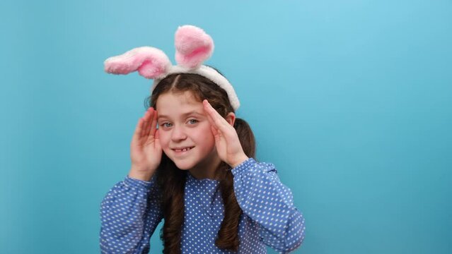 Portrait of cheerful laughing preteen girl in pink bunny ears playing peek boo game, happy child cover face with hands peeking having fun laughing, funny looking at camera, isolated on blue background
