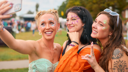 Three Female Friends Wearing Glitter Posing For Selfie At Summer Music Festival