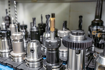 A tap for cutting threads in the hole of parts on a CNC machine against the background of other cutters and tools.