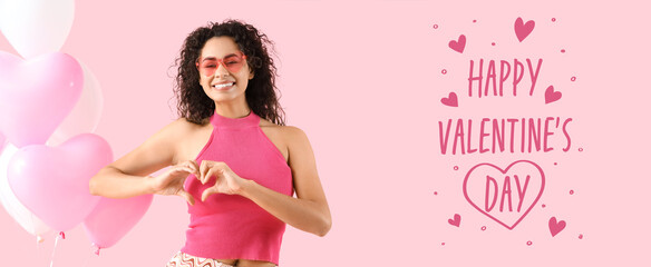 Happy young woman with heart-shaped balloons making heart with her hands on pink background. Banner...