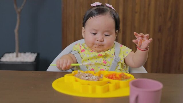 Little girl grabbing food with her hands while eating while sitting at the table at home. Supplementary feeding