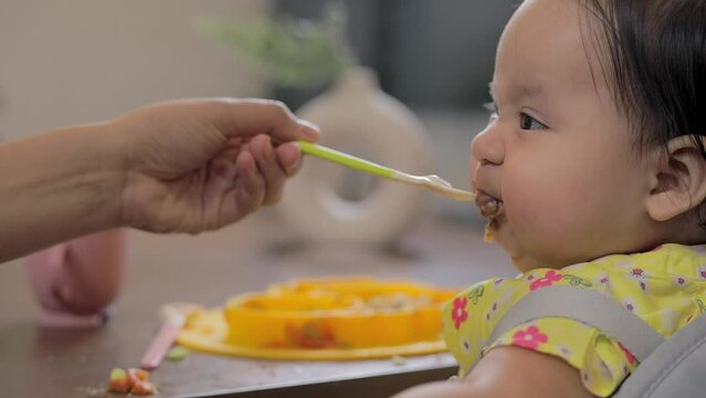 A baby turns to the camera while being spoon-fed