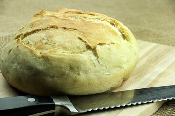 Freshly baked white bread from white flour, on a cutting board and a knife for slicing bread.