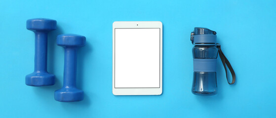 Modern tablet computer with blank screen, dumbbells and bottle of water on blue background