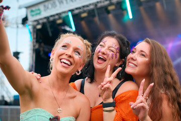 Three Female Friends Wearing Glitter Posing For Selfie At Summer Music Festival Holding Drinks