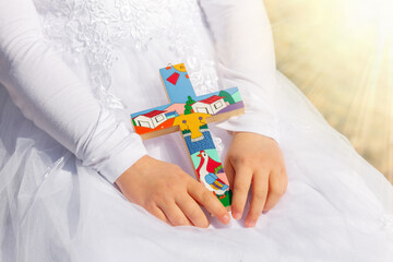 A wooden cross in the hands of a girl on the day of first communion, baptism. Traditions in...