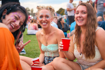 Portrait Of Three Female Friends Wearing Glitter Having Fun At Summer Music Festival Holding Drinks