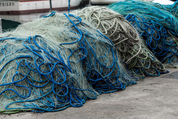 A series of fishing nets piled up on the harbor near fishing boats after a fishing trip. Nets...