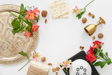 Frame made of Passover Seder plate, flatbread matza, kippah, wine cup, walnuts and flowers on white background