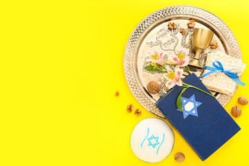 Composition with Passover Seder plate, flatbread matza, Torah, kippah and flowers on yellow background