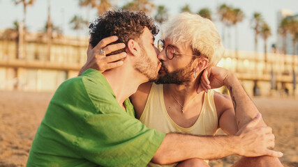 Close-up of young gay couple sitting hugging on the beach, smiling, talking and kissing