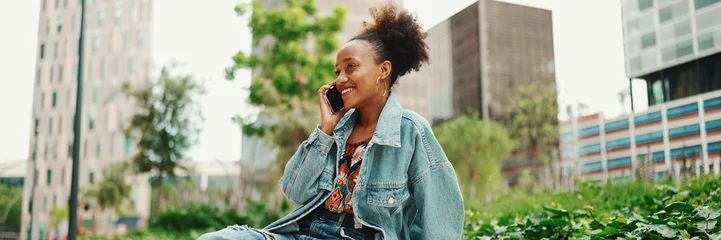 Fotobehang Closeup portret cute African girl with ponytail, wearing denim jacket, sits with morning coffee and makes stream, video call on modern city background. © Andrii Nekrasov