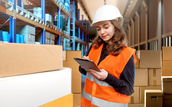 Woman inside warehouse. Storekeeper girl stands near boxes. Warehouse manager with tablet computer. Multi-tiered racks with paltas behind woman. Storekeeper smiles while doing work.