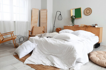 Interior of messy bedroom with bed, armchairs and pillows