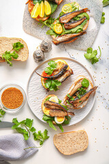 Plate and board of tasty sandwiches with canned smoked sprats on white marble background