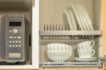 Plates for food inside cabinet. Kitchen utensils. Close-up microwave oven. Shelves for plates...