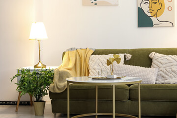 Interior of stylish living room with cozy green sofa, coffee table and glowing lamp