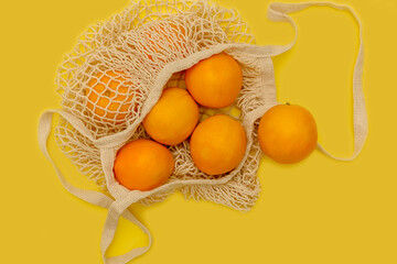 Orange oranges in a cotton string bag. On a yellow background. Sweet fruits.