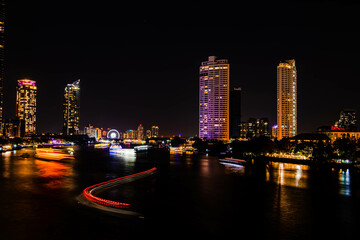 Fototapeta na wymiar Night light landscape along the Chao Praya River, having some boats come to celebrate the New Year eve on the Asiatique landmark side in Bangkok city, Thailand.