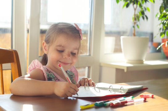 Cute smiling little girl drawing with multicolor gel pens at home, kid enjoying creative activity