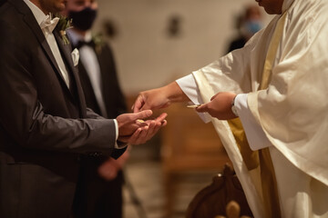 Ein Pfarrer reicht dem Bräutigam während der Trauung eine Hostie. - obrazy, fototapety, plakaty