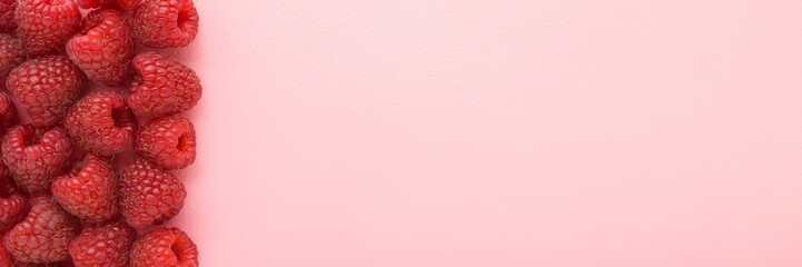 Row of fresh red raspberries on light pink table background. Pastel color. Wide banner. Closeup....