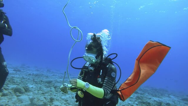 still view of a female woman scuba diving instructor wearing gear regulator fine mask BCD equipment demonstrates how to tie a node from lift bag underwater during teaching course in blue ocean water