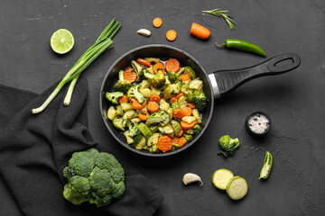 Frying pan with tasty vegetables on black background