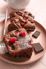 Plate with pieces of raspberry chocolate brownie on pink tile table