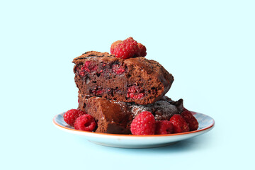 Plate with pieces of raspberry chocolate brownie on blue background
