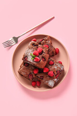 Plate with pieces of raspberry chocolate brownie on pink background