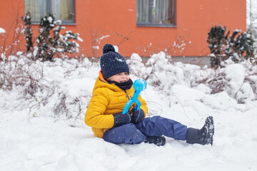 Fototapeta na wymiar Winter games outdoors. Small boy have fun making snowballs with toy plastic maker.