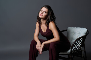 Fototapeta na wymiar Fashionable young woman posing sitting in chair on dark gray studio background