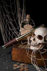 Pirate chest with spyglass, human skull, bottle of rum and coins on black background
