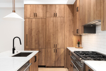 A kitchen detail with wood cabinets, black faucet, a bronze light fixture hanging above the white...