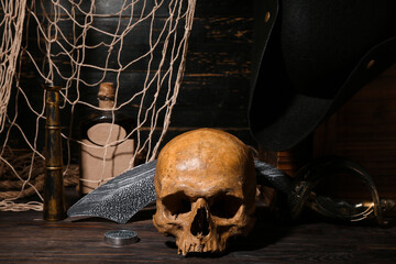 Human skull with bottle of rum, sword and spyglass on brown wooden background