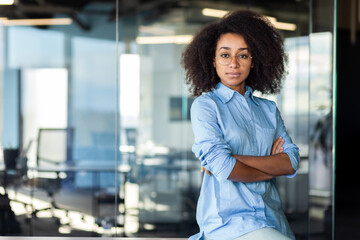 Portrait of a confident African-American young business woman sitting in the office at the desk,...