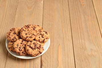Plate of tasty cookies with chocolate chips on wooden background