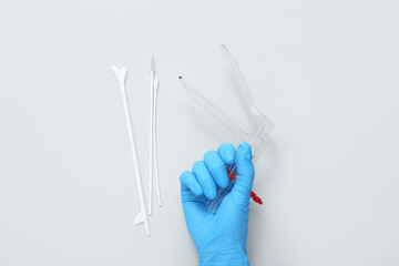 Hand in medical glove, with gynecological speculum and pap smear test tools on light background