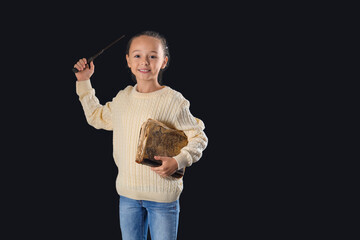 Cute little girl with adventure book and magic wand on dark background