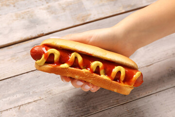 Woman holding tasty hot dog on grey wooden background