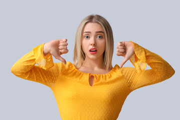 Upset young woman showing dislike on light background