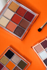 Colorful eyeshadow palettes and make up brush on orange background. Top view. 