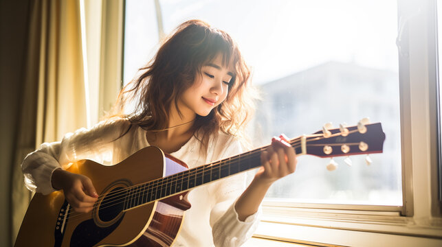 A young teenager playing an acoustic guitar by the window with sunlight streaming in.
