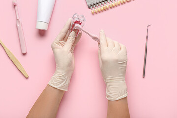 Dentist with plastic tooth and brush on pink background, top view
