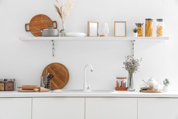 Interior of modern kitchen with white counters, shelf, sink and utensils